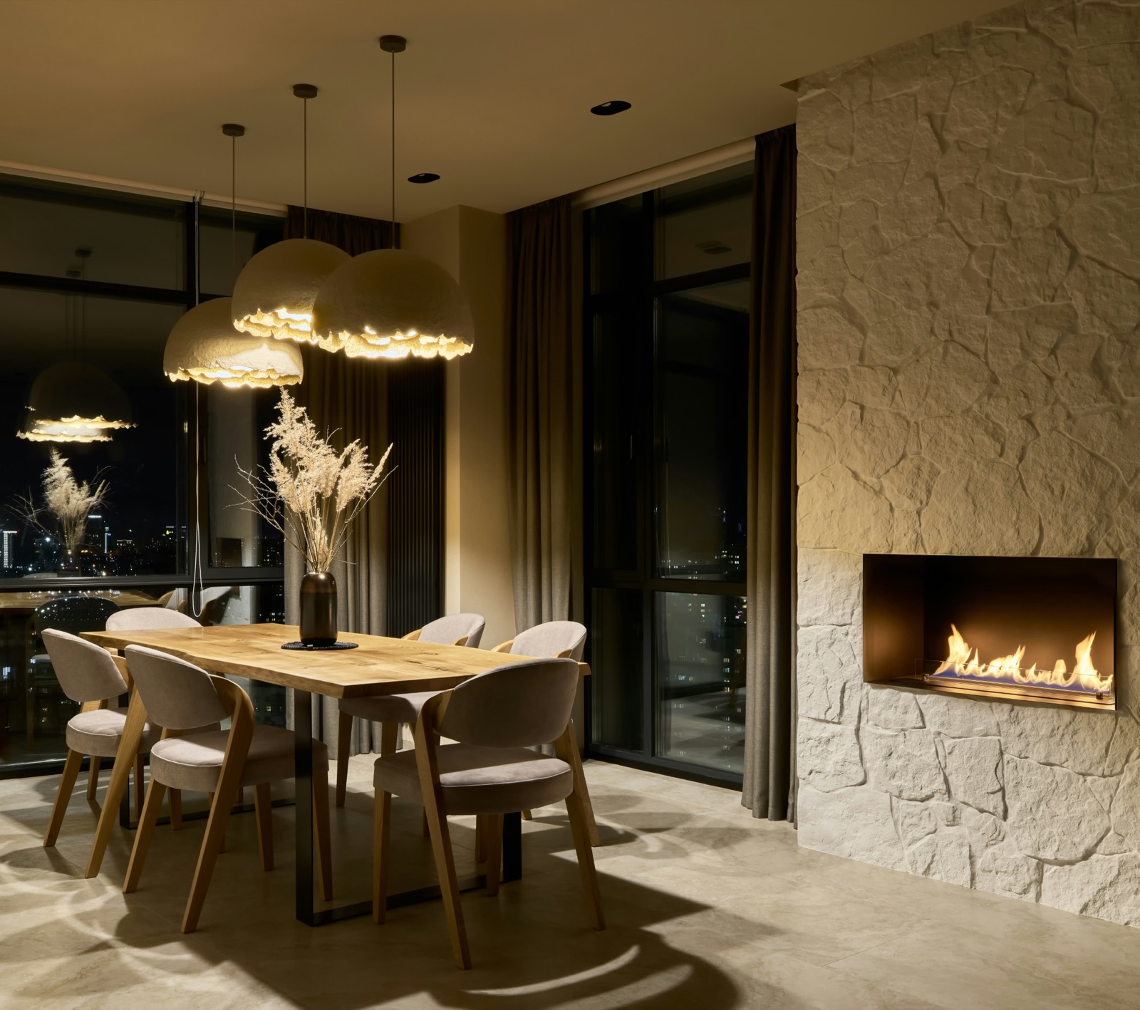 A warm dining room with a fireplace and city views at night